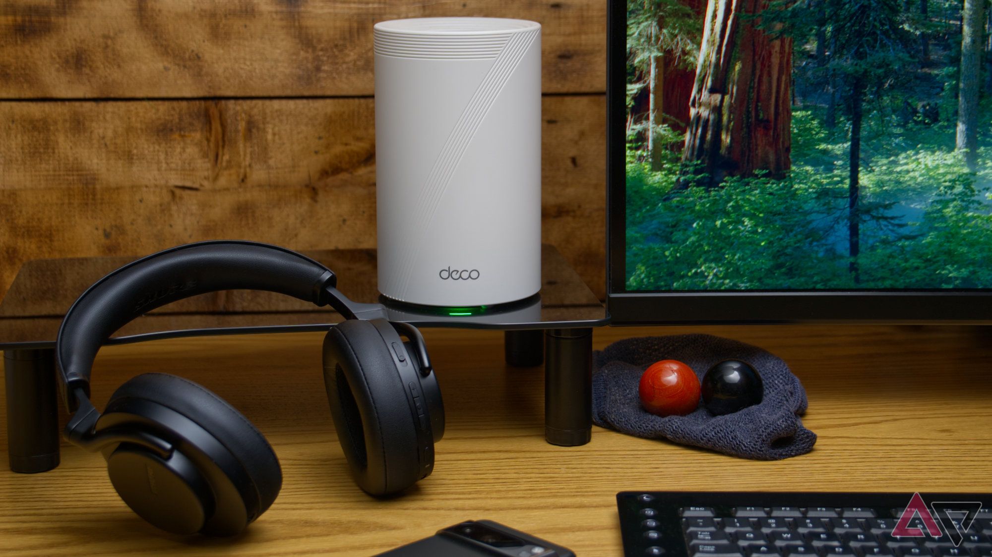 TP-Link Deco BE65 Pro sitting on a desk stand next to several other items with a wooden background