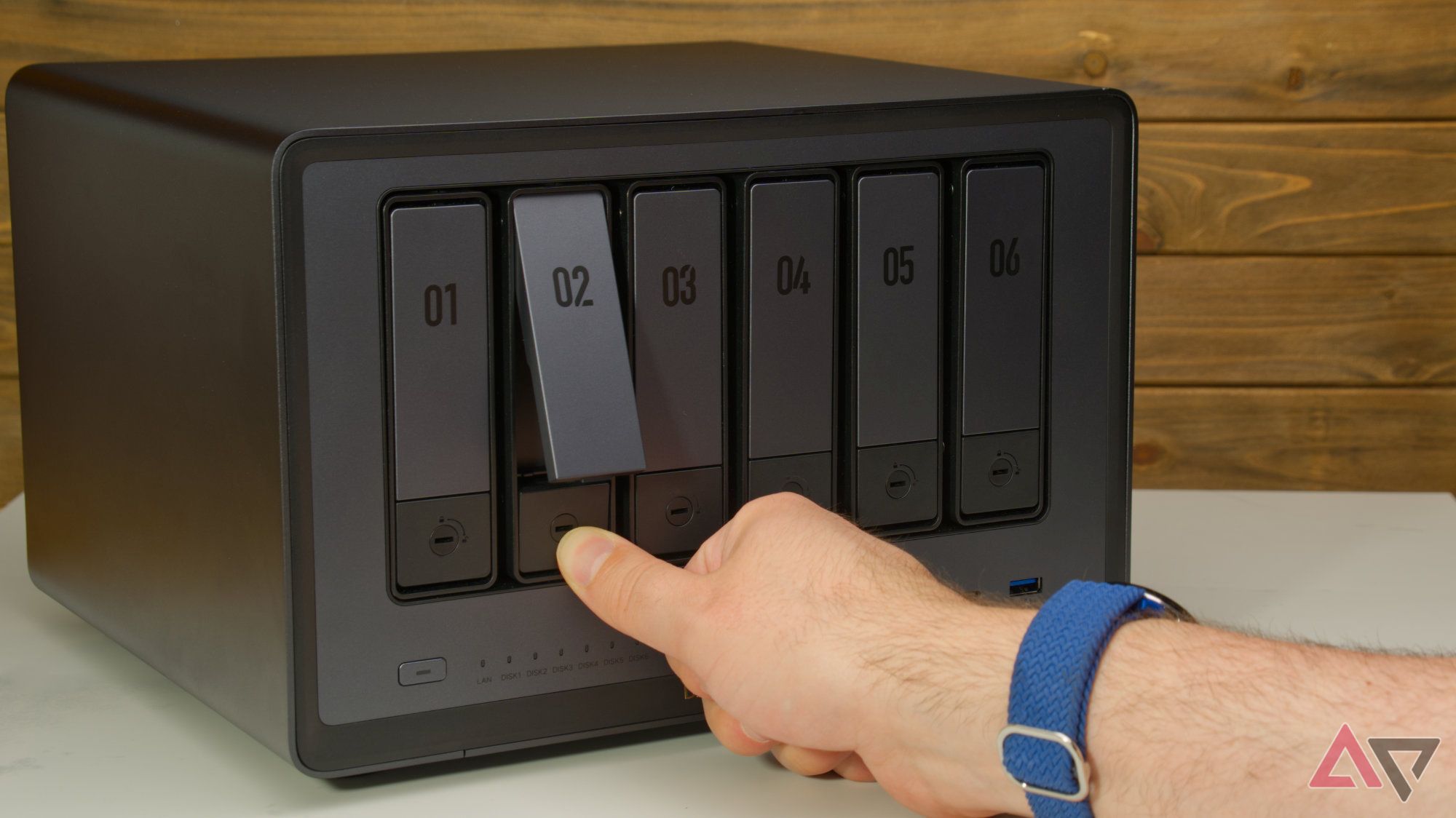 Ugreen DXP6800 Pro on a desk while a hand presses the handle release on a drive caddy