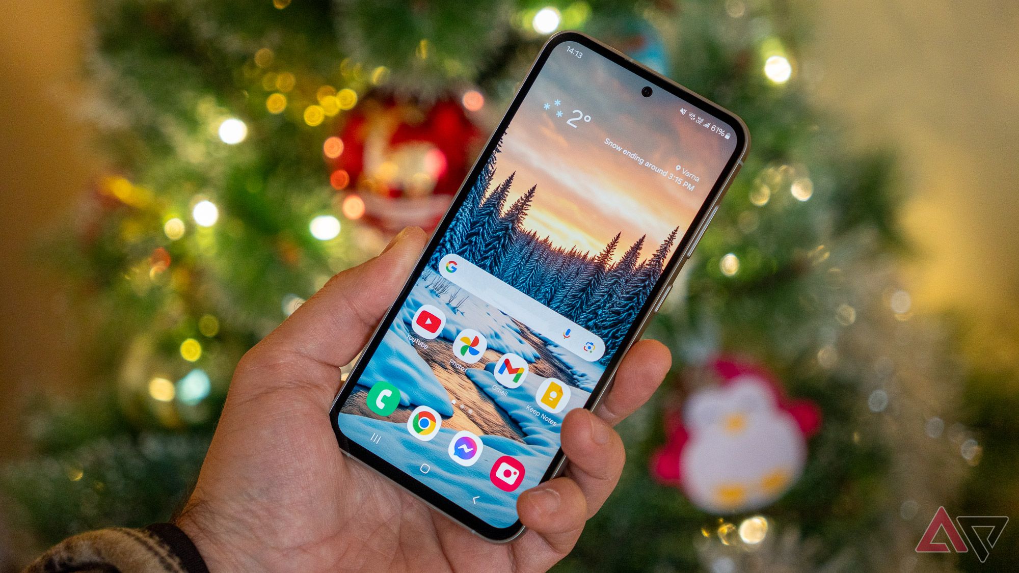 a phone on the home screen held in hand in front of a christmas tree 