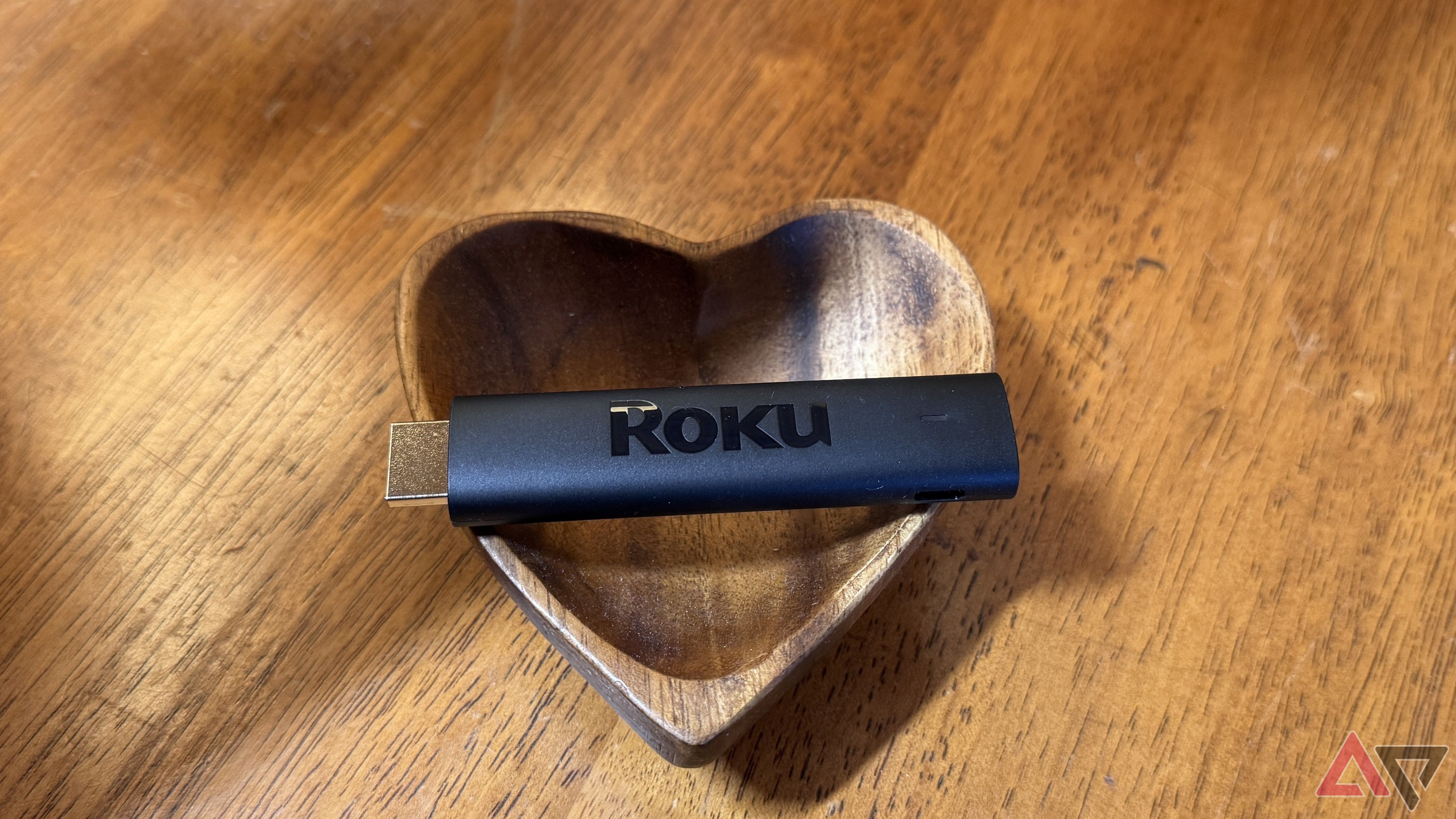 Roku Streaming Stick 4K on resting horizontally on a wooden heart-shaped bowl.