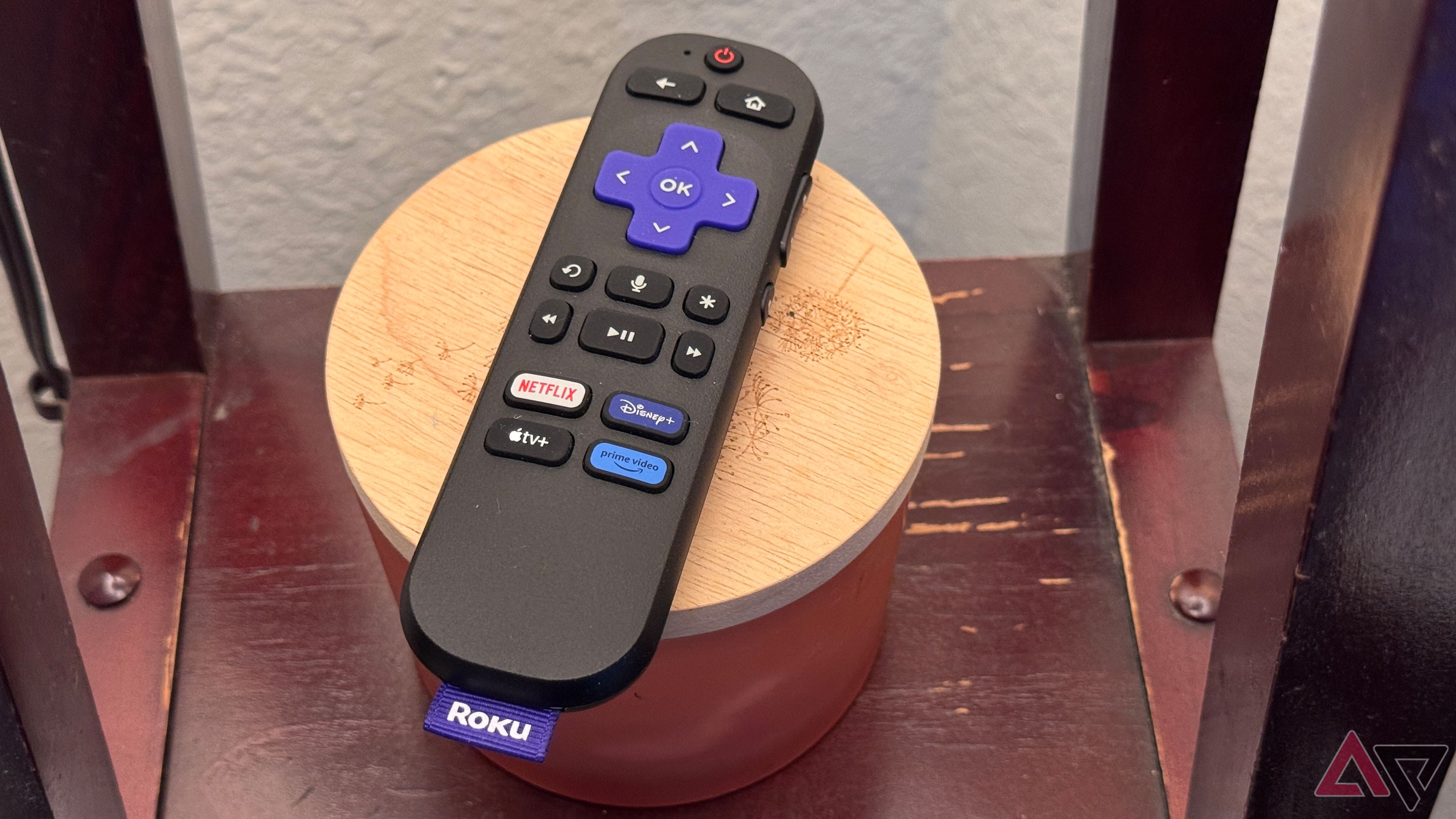 Roku Streaming Stick 4K Remote on candle jar with a light wooden top which is resting on a wooden shelf.