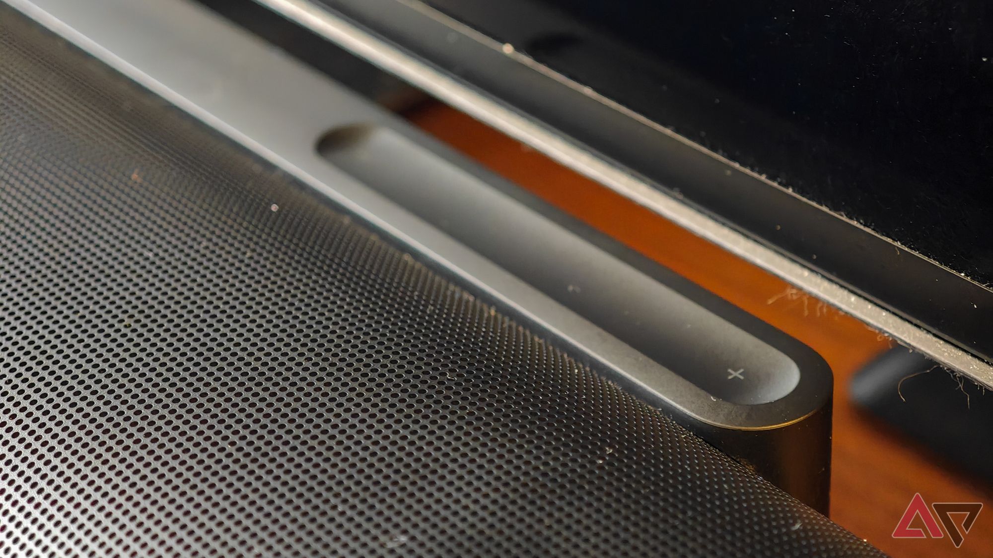 Black Sonos Arc Ultra soundbar resting on a teak wooden cabinet, focussing on the volume slider control