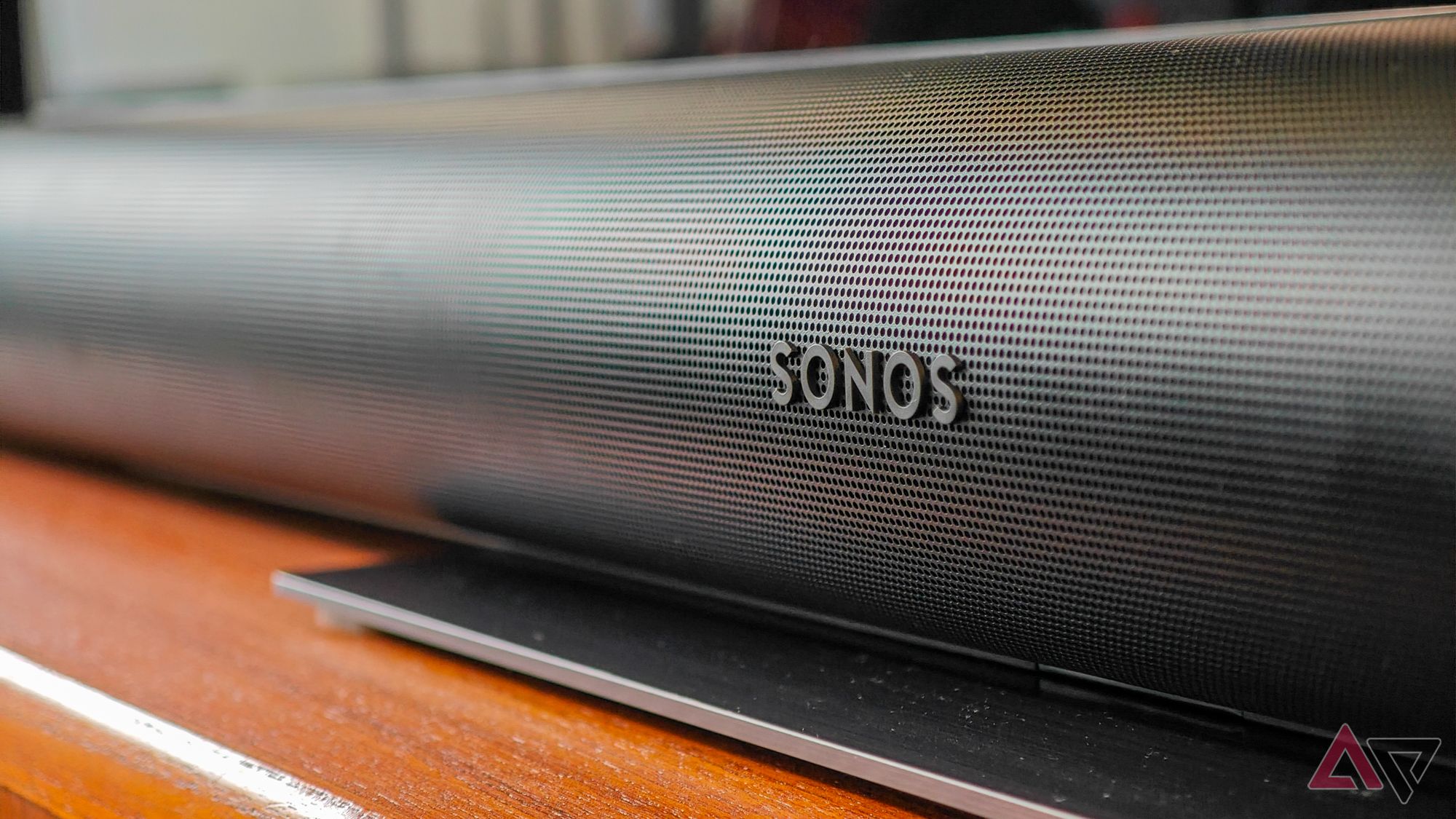 Black Sonos Arc Ultra soundbar resting on a teak wooden cabinet, focussing on the Sonos logo on the front