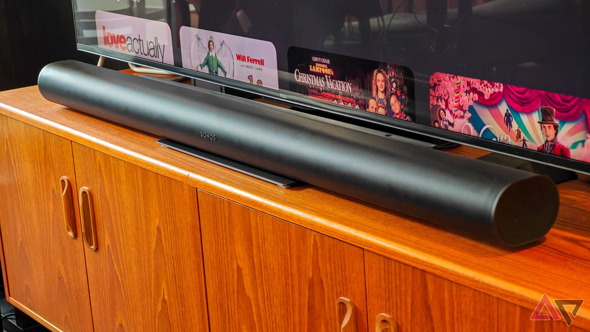 Black Sonos Arc Ultra soundbar resting on a teak wooden cabinet