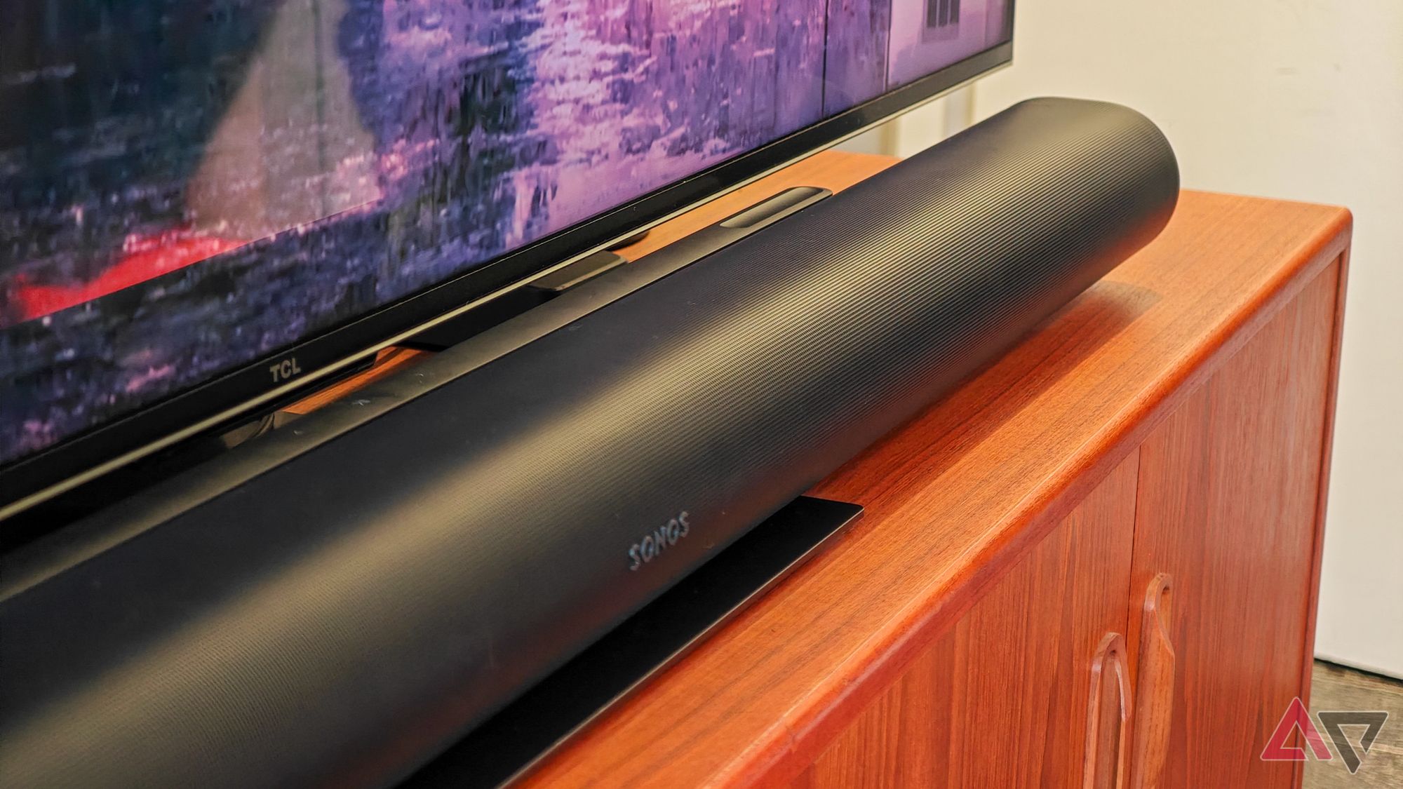 Black Sonos Arc Ultra soundbar resting on a teak wooden cabinet