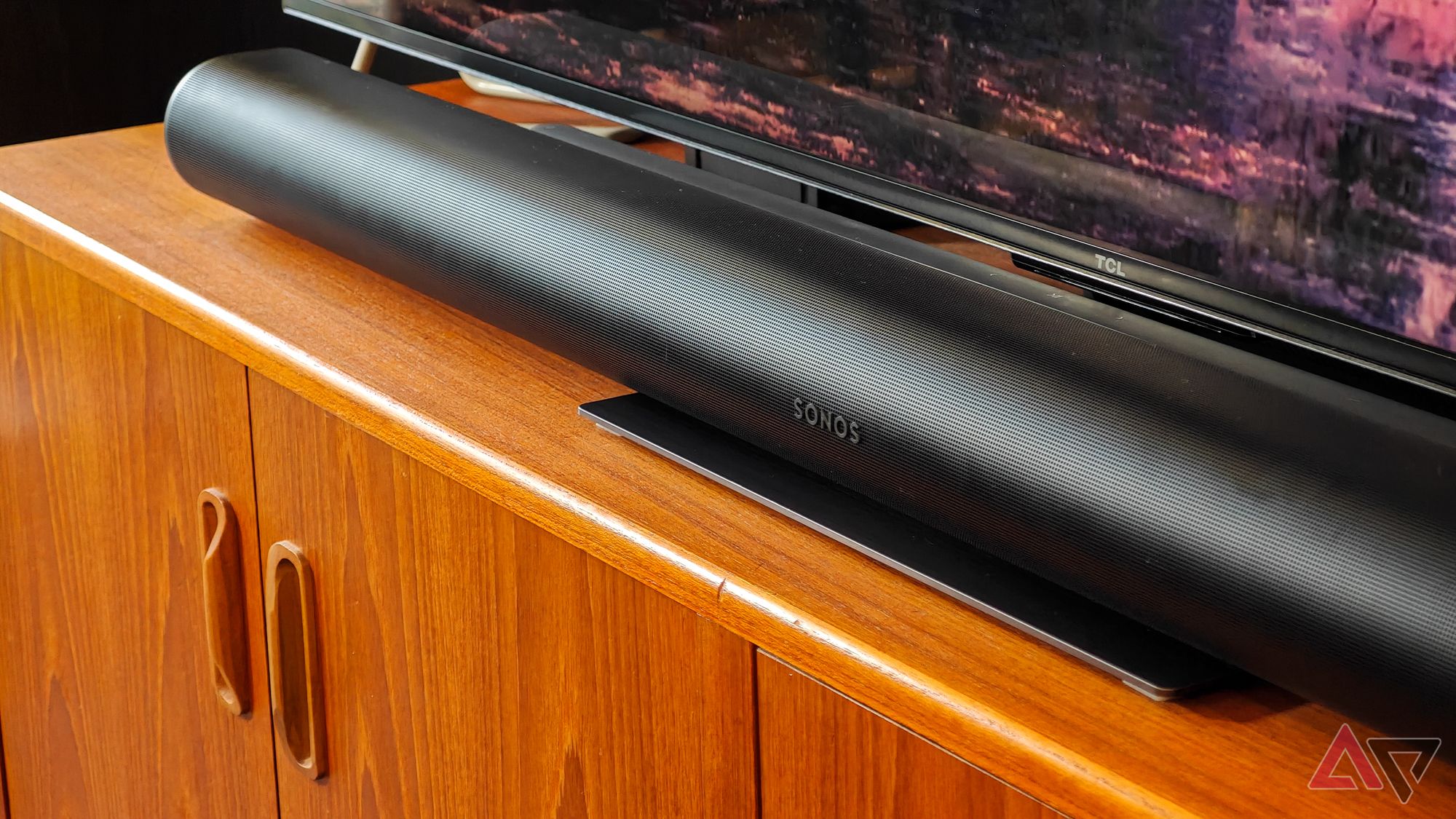 Black Sonos Arc Ultra soundbar resting on a teak wooden cabinet