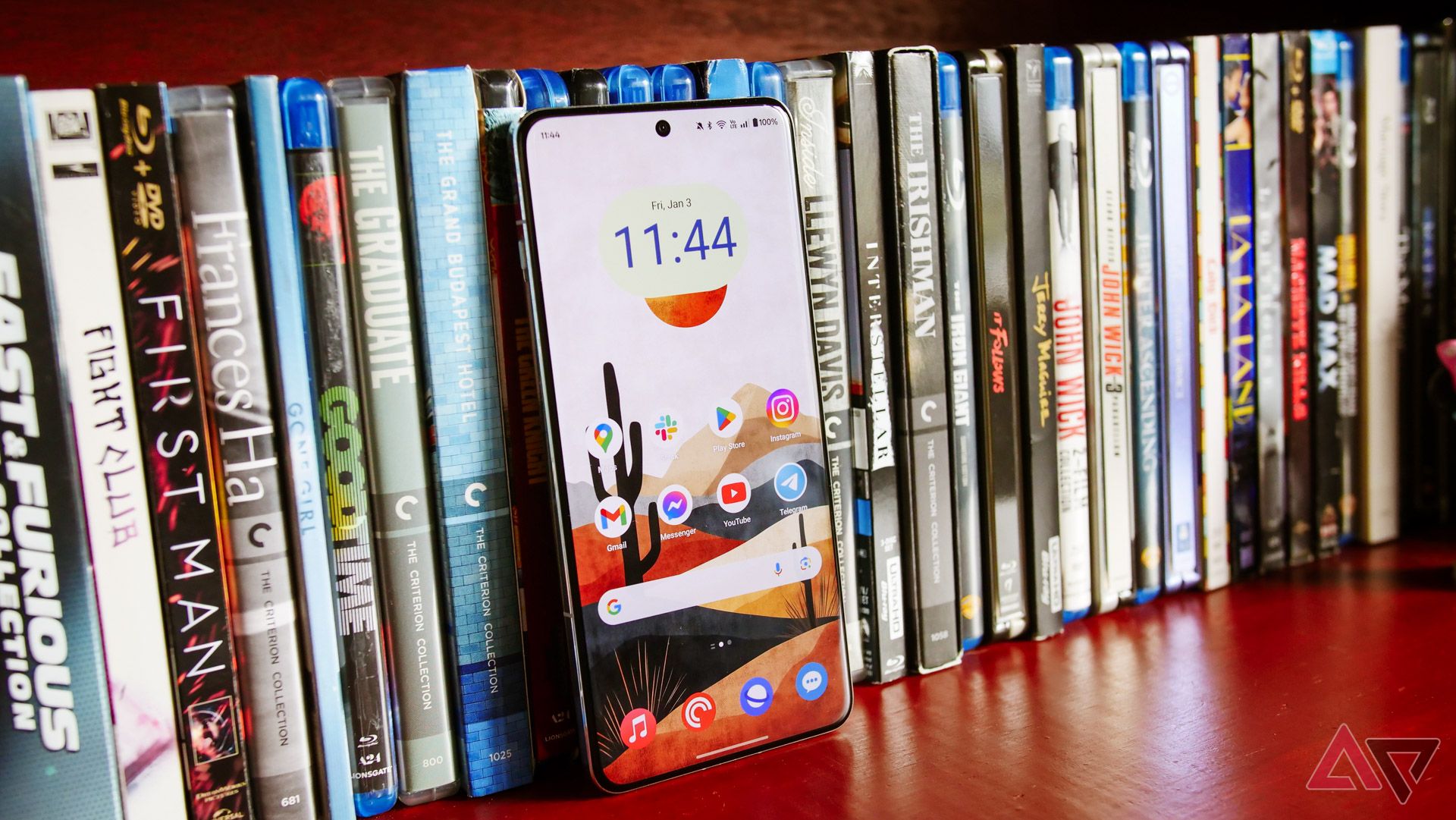 The OnePlus 13 on a bookshelf filled with movies.