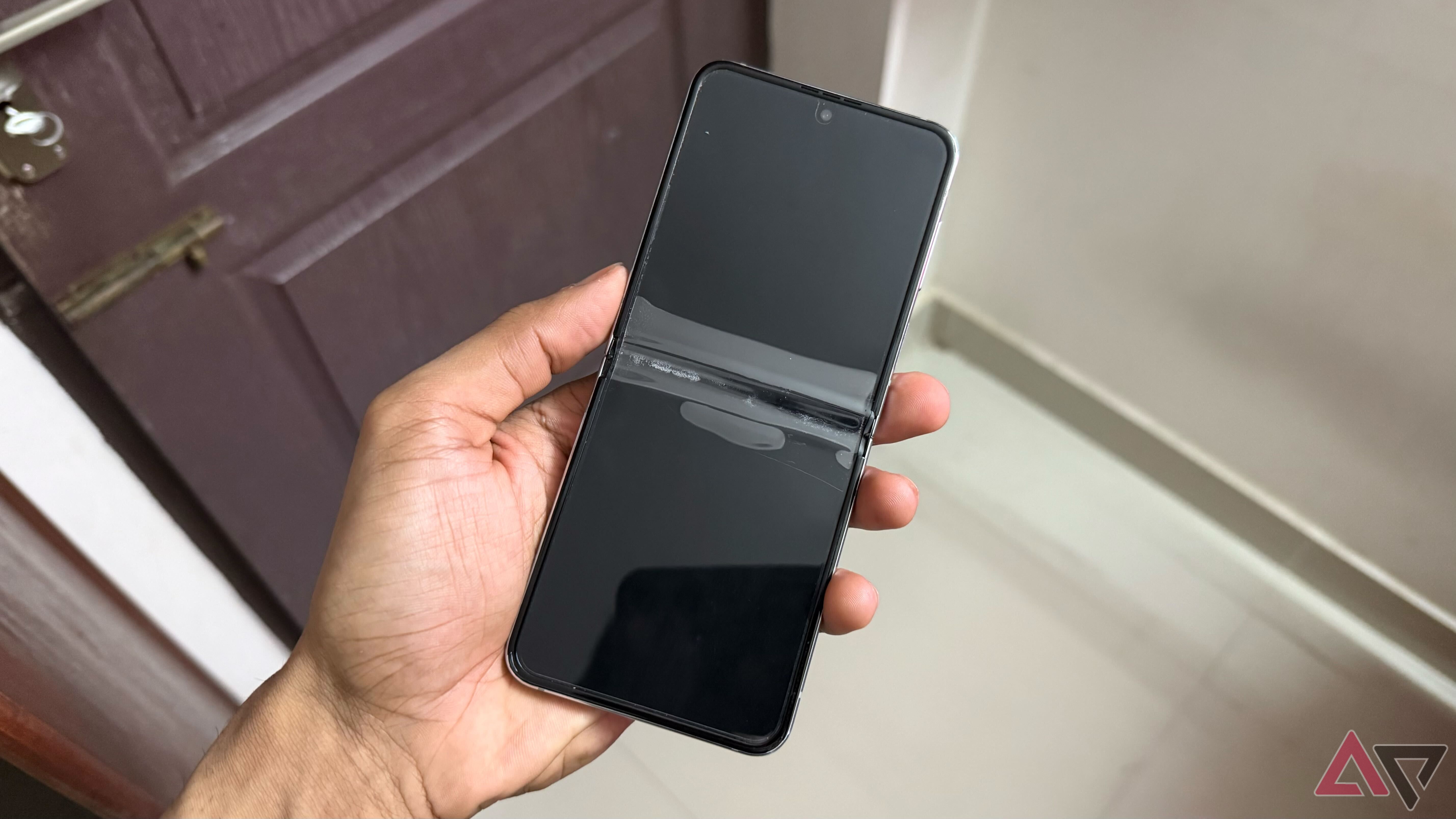 A man holding an old Samsung Galaxy Z Flip 5 with screen protector coming off