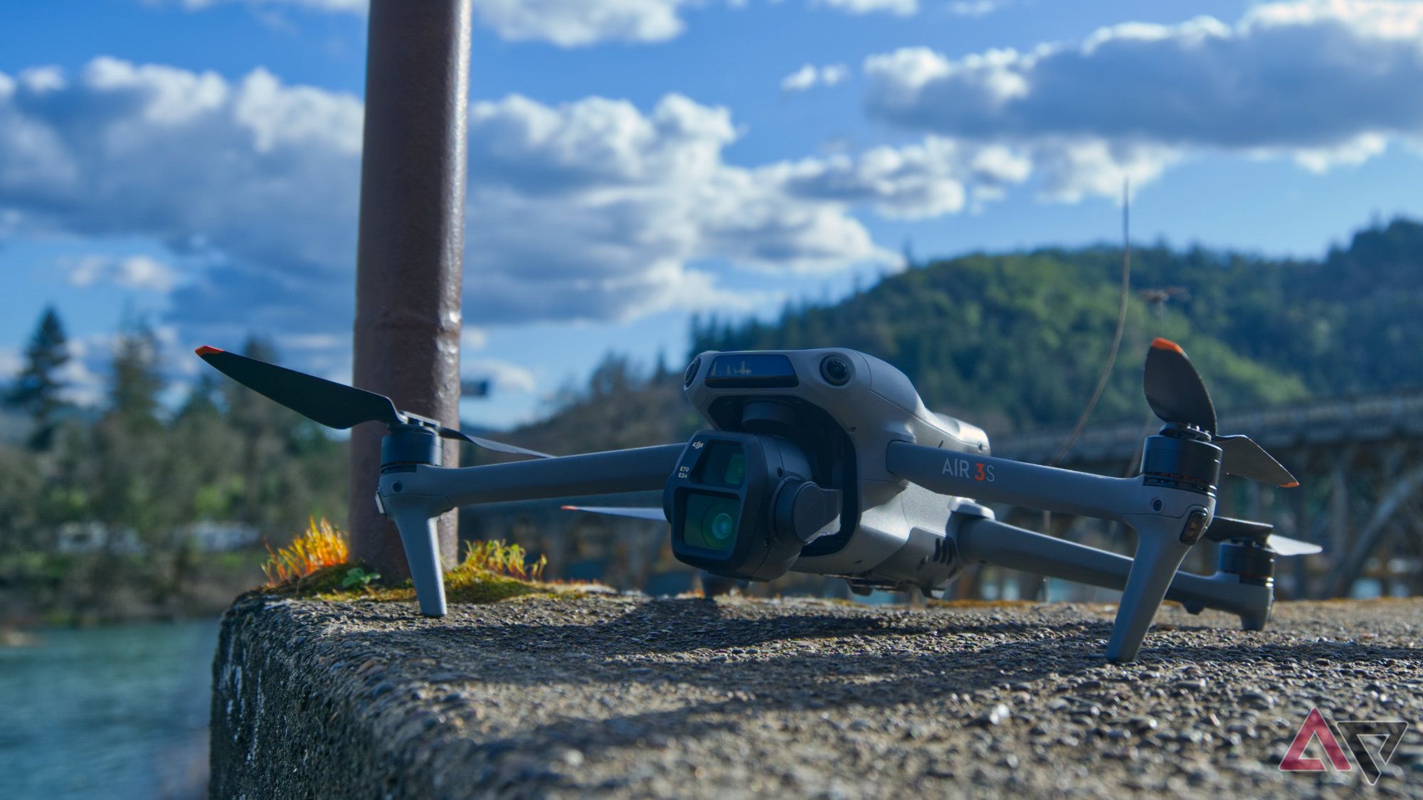 Up angle shot of a DJI Air 3S with a river, mountain, and clouds in the background