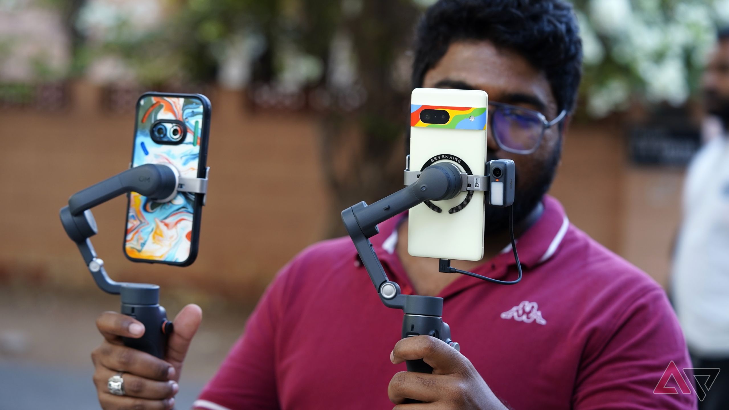 DJI Osmo Mobile 7 Pro held alongside a Mobile 6 with an orange wall in the background