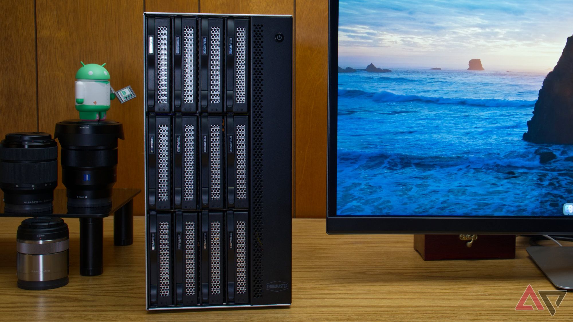TerraMaster T12-500 Pro on a desk next to a monitor, a shelf with camera lenses, and an android figurine
