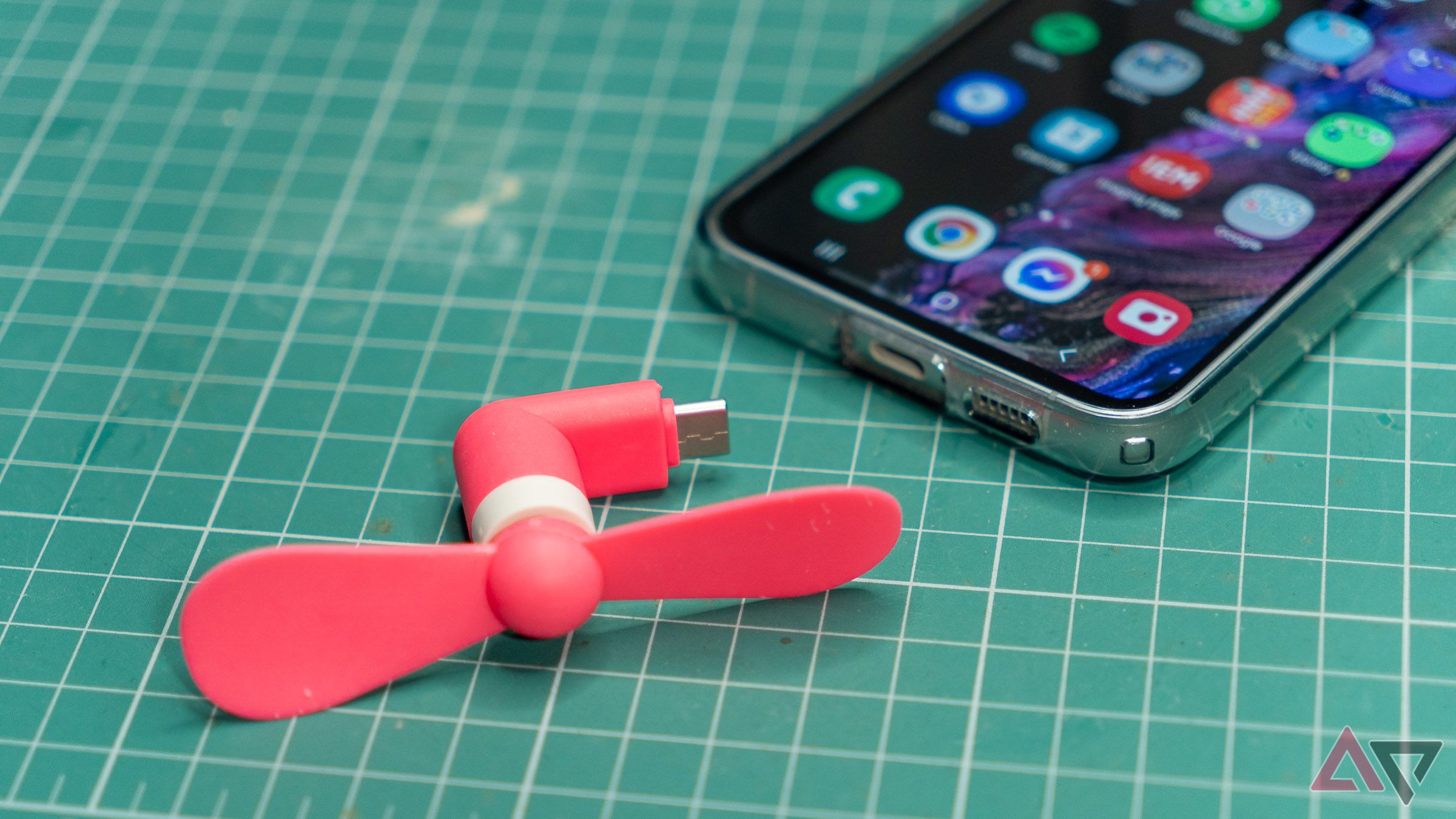 a pink usb fan next to a samsung phone on a green mat