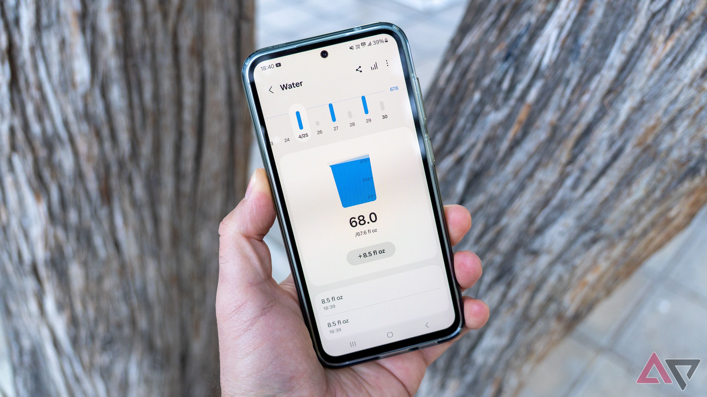 a phone in hand displaying water intake statistics with two trees in the background