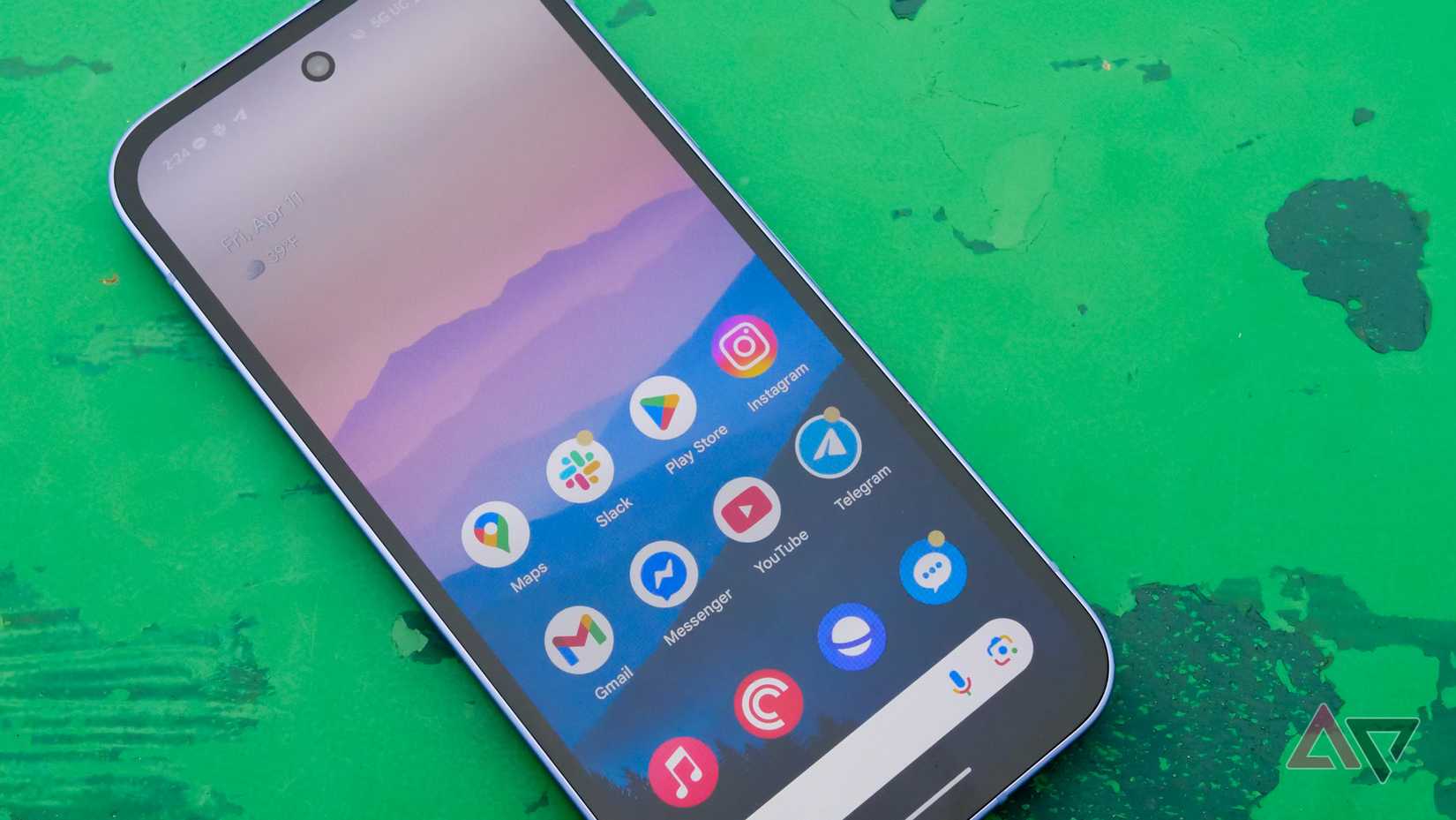 O Google Pixel 9A em uma mesa verde em um parque do lado de fora, com a tela ligada e para cima