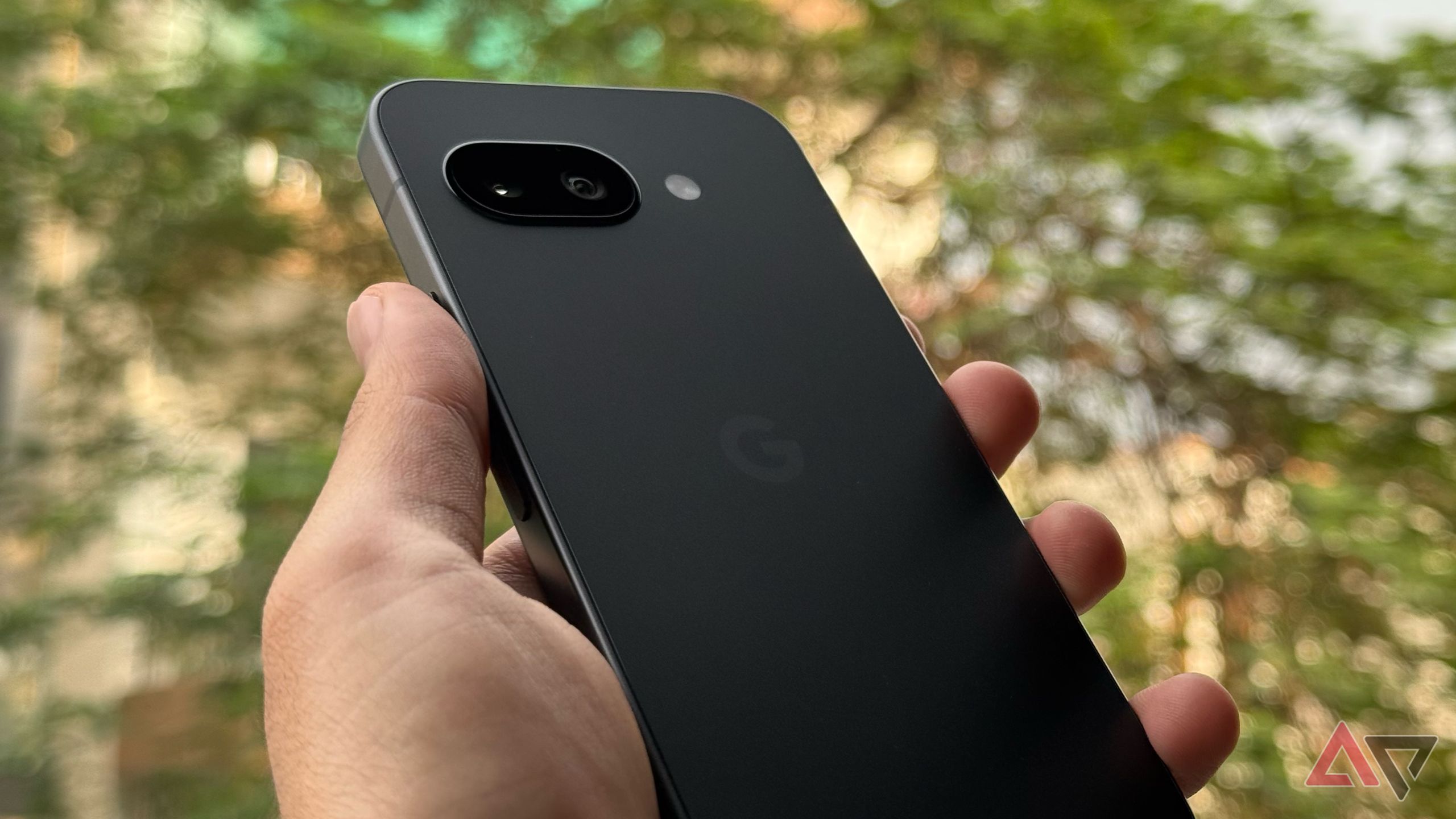 Angled shot of black Pixel 9a held up outdoors showing the back design