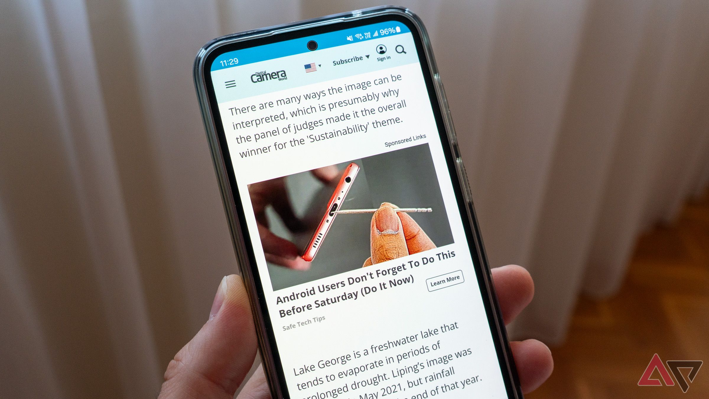 a phone in hand displaying a website and an advertisement against a curtain in the background