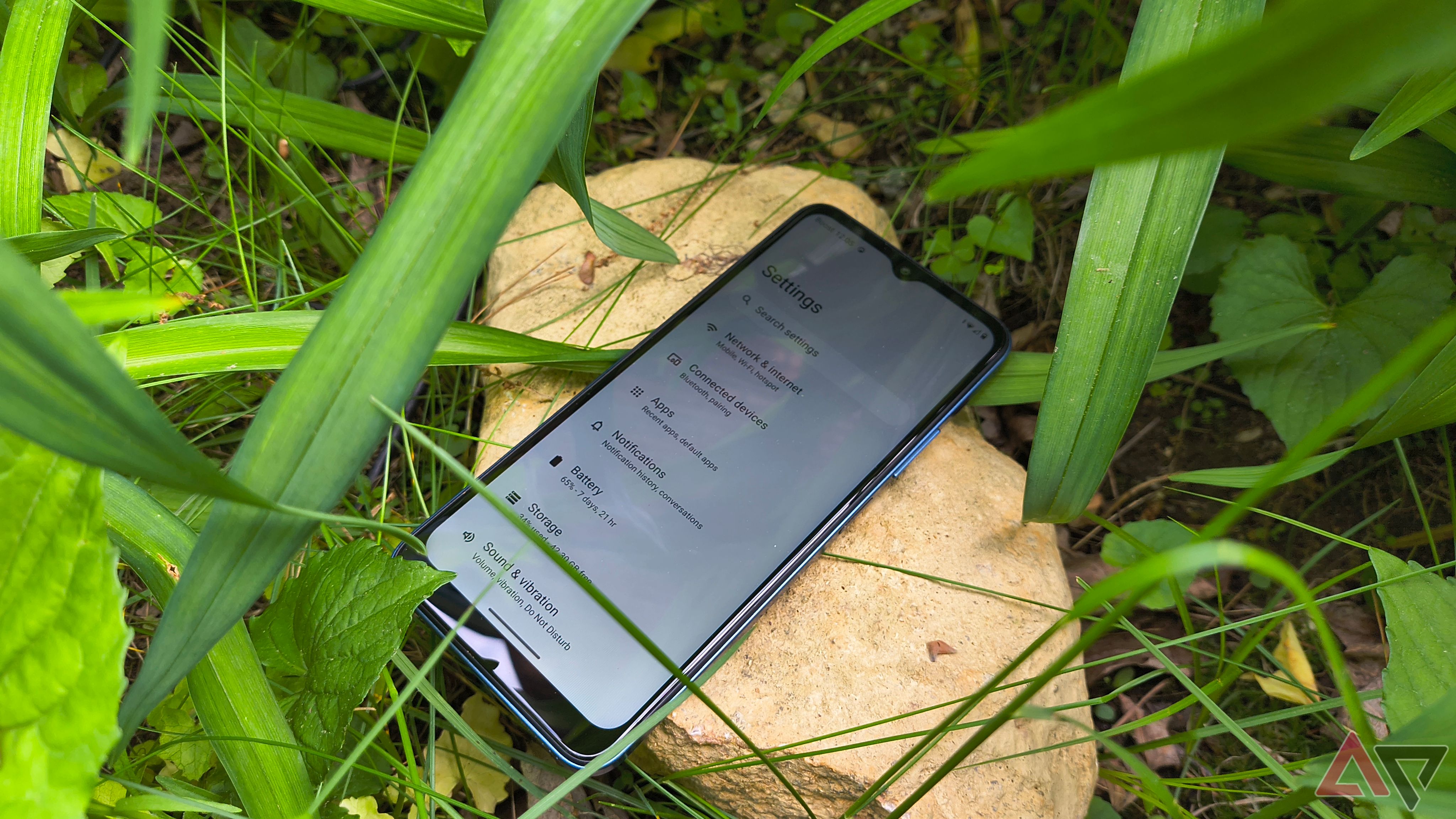 A Boost Summit 5G phone sitting face up on a rock in some plants with the settings screen visible