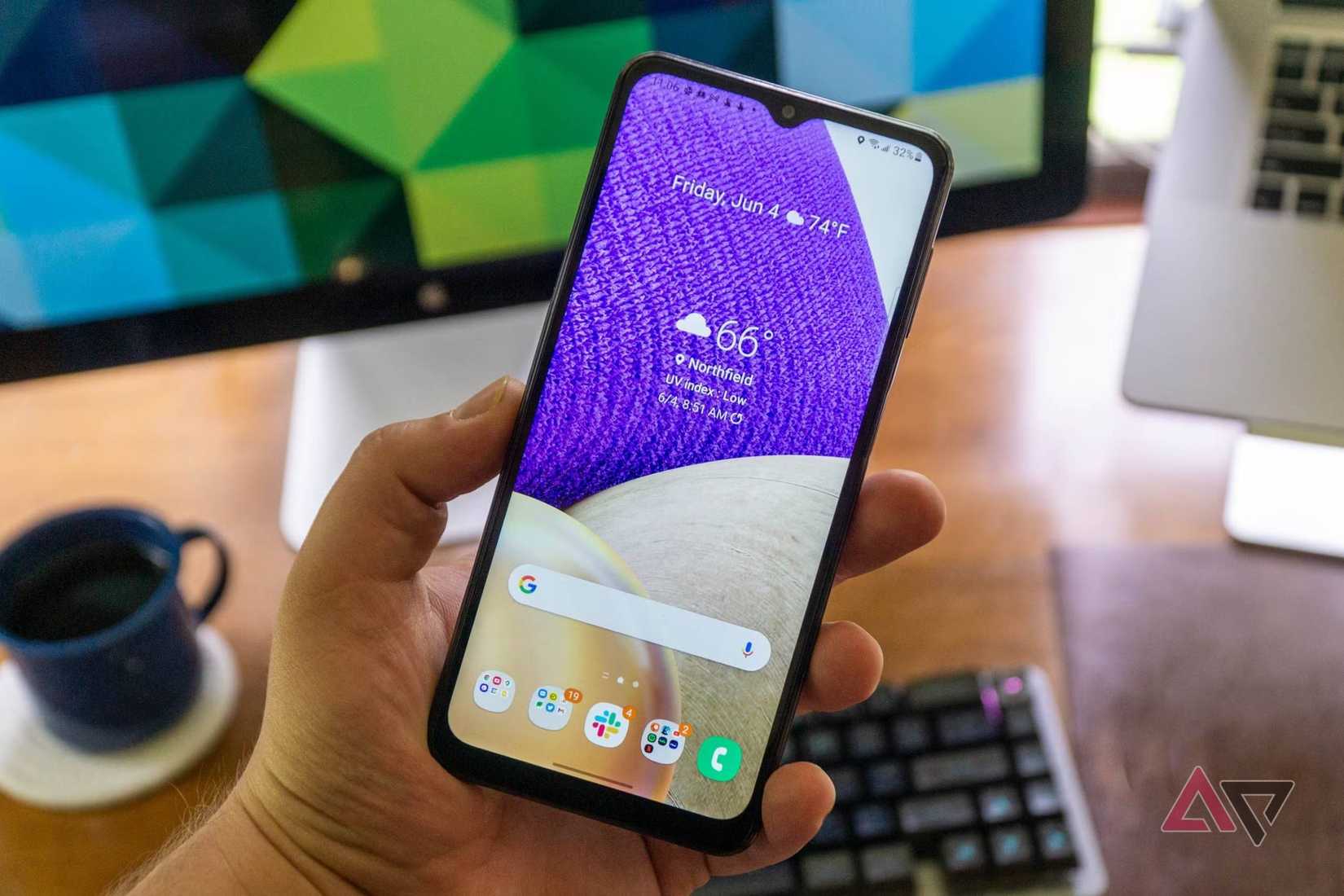 The Galaxy A32 held in a hand in front of a computer desk.